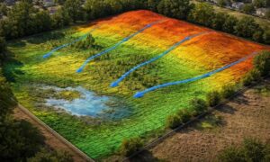 Realistic LiDAR mapping terrain visualization showing elevation changes and drainage flow across a construction site with colored slope gradients and water direction patterns