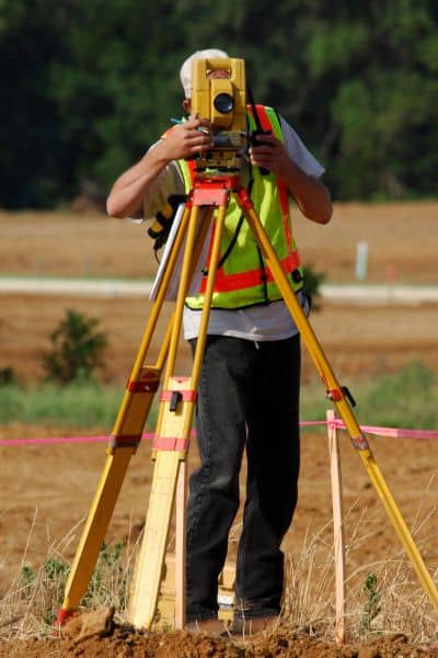 Licensed land surveyor using a total station during a boundary survey on a residential property to measure and verify property lines