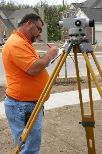 Surveyor measuring ground levels in a residential neighborhood to assess drainage issues that often lead homeowners to search for engineering consultants near me